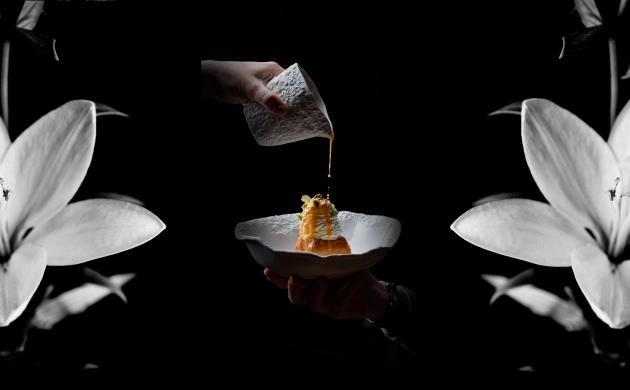 Dessert raffiné nappé de sauce, entouré de fleurs blanches pour une présentation élégante et artistique.