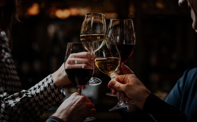 quatre personnes trinquent avec des verres de vin rouge et blanc dans un cadre chaleureux, probablement un bar ou un restaurant.