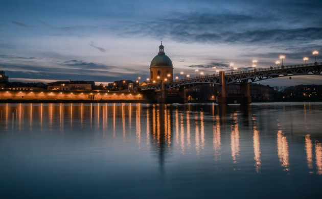 Pont illuminé au crépuscule se reflétant sur la Garonne à Toulouse, créant une ambiance paisible et romantique.
